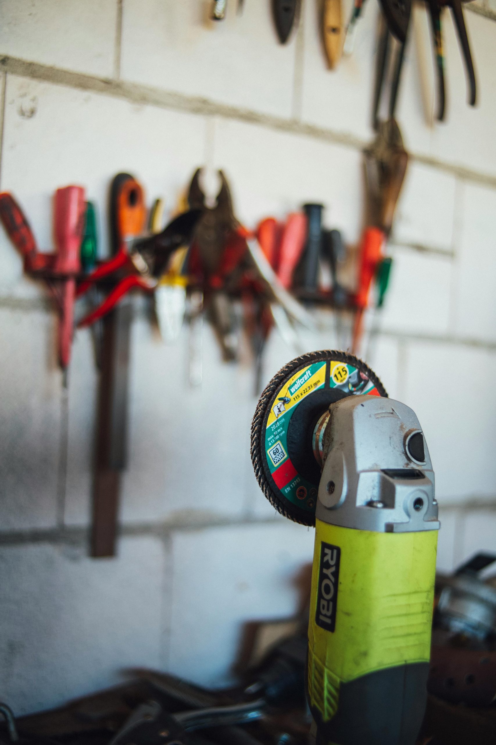 Close-up of a power tool with various tools hanging on a workshop wall.